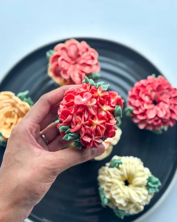 Holding up a detailed red hydrangea cupcake, crafted entirely from buttercream.