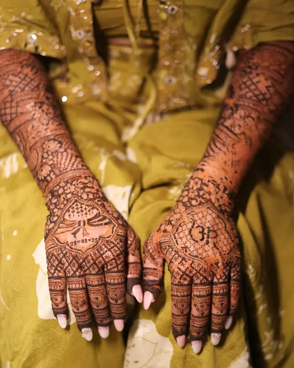The complete bridal look, with both hands adorned in intricate, personalized mehendi. This design features portraits, initials, and traditional patterns.