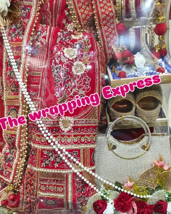 A close-up of a beautifully packed red bridal lehenga. You can see the detailed embroidery, and I've arranged the matching handbag, juttis, and bridal chooda to create a complete and impressive gift set.