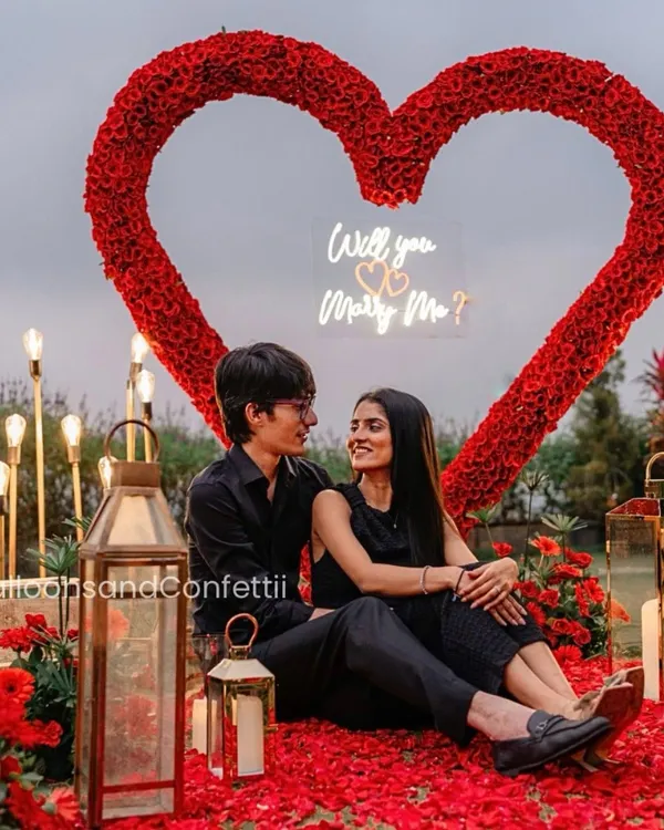 The ultimate romantic gesture. This proposal setup features a custom-made heart archway using over 2,000 fresh red roses, a petal-strewn floor, and a neon "Will you Marry Me?" sign for a truly unforgettable moment.