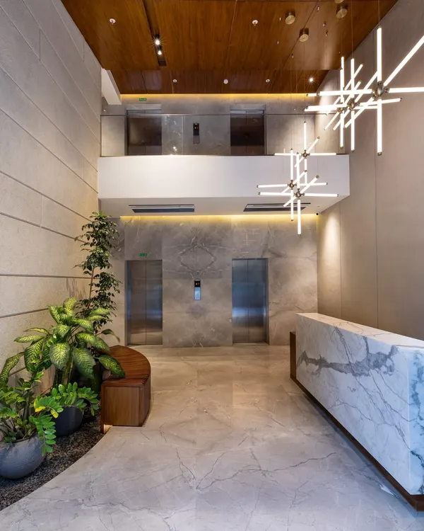 This lobby is a statement of quiet luxury, where bold marble, warm wood, and lush greenery come together in a balanced composition. The double-height space and sculptural chandelier are designed to elevate the arrival experience and establish a distinct spatial identity.