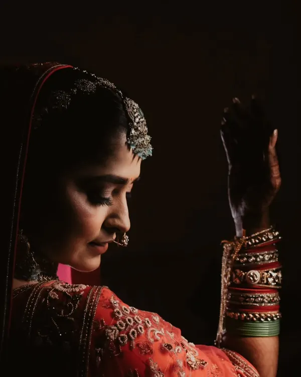 In the quiet moments before the ceremony, a bride's portrait is a story of anticipation. This low-light, artistic shot captures her grace and the intricate details of her attire.