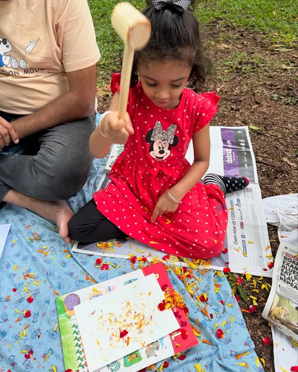A young artist completely absorbed in the process of flower pounding. With a wooden mallet in hand, she is learning how to transfer the vibrant colours of marigold petals onto paper, creating her own unique masterpiece.