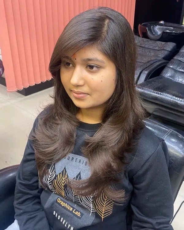 A beautiful feather-cut with side-swept bangs. This style is perfect for adding softness and volume around the face, creating a flattering and modern look.