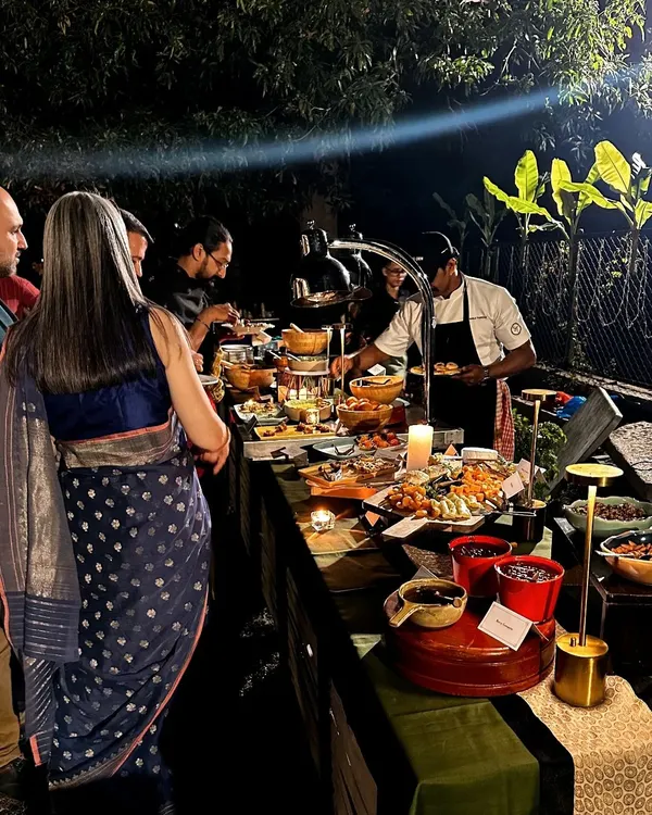 Guests enjoy a lavish spread at an outdoor evening event. A chef is seen serving directly from the beautifully lit buffet, showcasing the interactive and high-touch service that defines a Single Thread gathering.