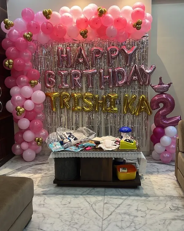 A fun and sparkly birthday setup in pink and gold. The silver fringe backdrop makes the 'Happy Birthday' foil balloons pop, and the balloon columns add a festive touch.