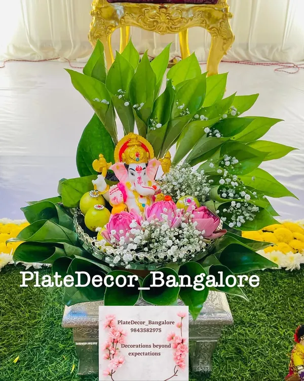 A beautiful pooja platter with a Ganesha idol placed on a bed of betel leaves, surrounded by lotus buds and baby's breath flowers.