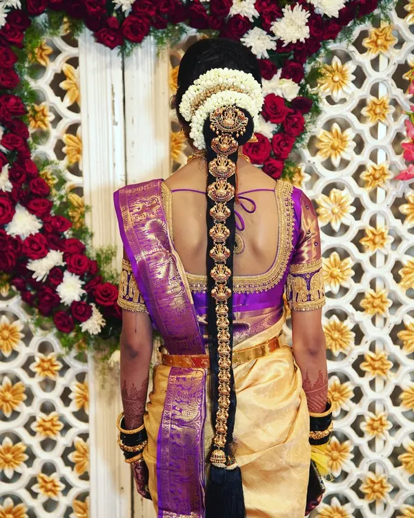 A stunning shot of a South Indian bride's traditional hairstyle, featuring an intricate hair braid ornament (Jadai Billai) and fresh flowers.