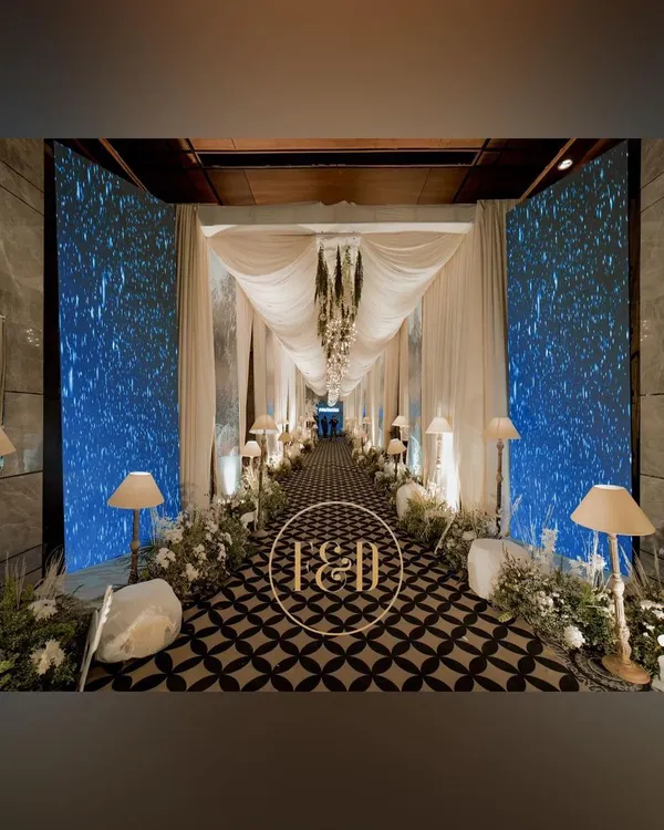This is how we make an entrance. A magical walkway designed for a winter-themed sangeet, using draped fabrics, custom geometric print flooring, and flanking LED screens that displayed a starry night sky, creating a truly immersive experience for the guests.