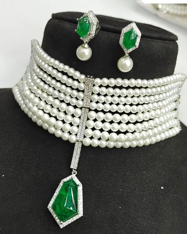 This modern multi-strand pearl choker features a central emerald green stone pendant. It comes with matching pearl drop earrings and is available for rent.