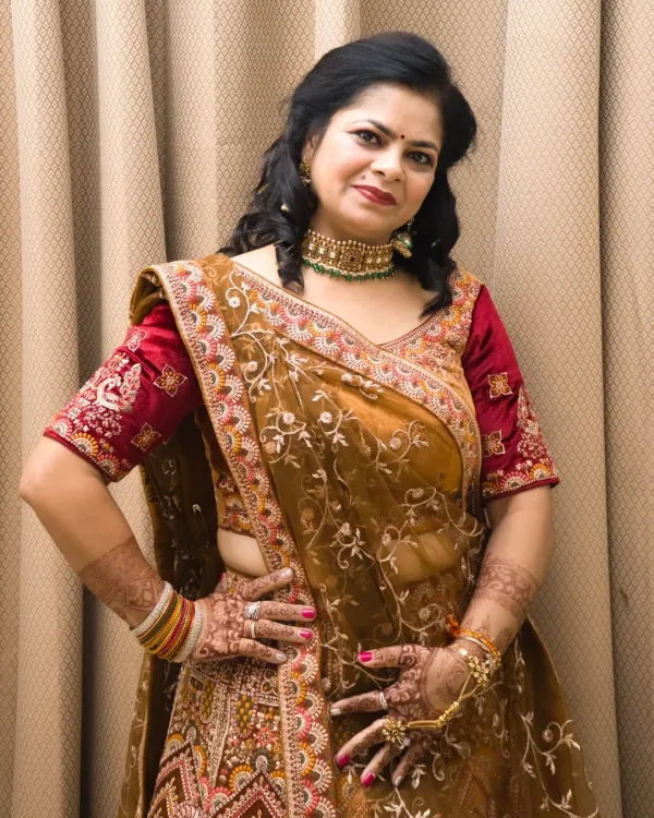 A confident pose in a beautiful mustard and red embroidered lehenga. This indoor shot highlights the intricate details of the outfit and the henna on her hands.