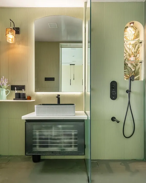 This bathroom is a serene retreat, wrapped in soft green fluted wall panels. I designed a custom niche in the shower with a tropical wallpaper backing for a surprise element. The floating vanity with a reeded glass front feels light and modern, complemented by the black matte fixtures.