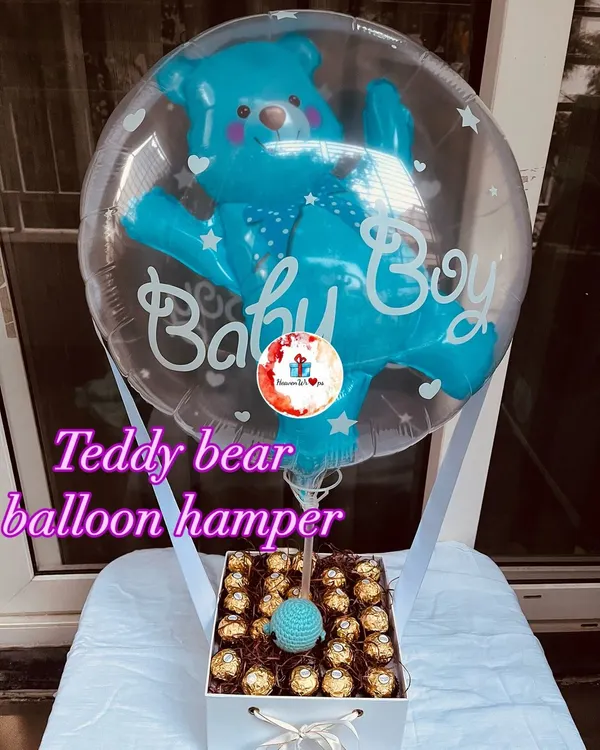 A stunning "Baby Boy" balloon hamper, featuring a transparent balloon with a blue teddy bear, floating above a box filled with Ferrero Rocher chocolates. This is one of my most popular designs for baby announcements and showers.