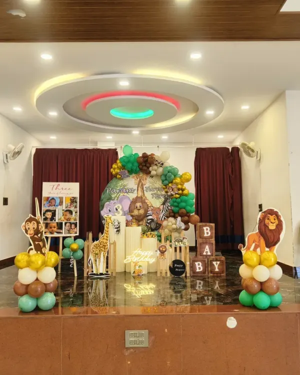 A grand jungle-themed birthday party on a stage, featuring a large balloon arrangement, animal cutouts like a lion and giraffe, and a personalized photo easel.