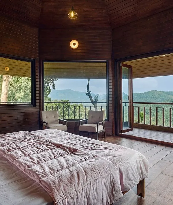 This bedroom in a rustic-luxury home is designed to be a private retreat with a connection to nature. We used wood-paneled walls and flooring to create a warm, cabin-like feel, with large windows and a private balcony that open up to stunning mountain views.