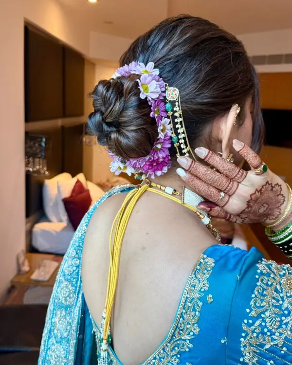 A detailed shot of a classic bridal bun, adorned with a mix of purple and white flowers and a traditional hair accessory. This style is perfect for securing a heavy dupatta.