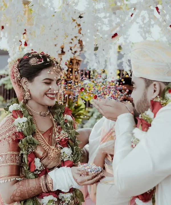 A candid shot of the groom showering the bride with blessings and rice during the ceremony. It’s a moment of pure joy and tradition, captured under a beautiful floral mandap.