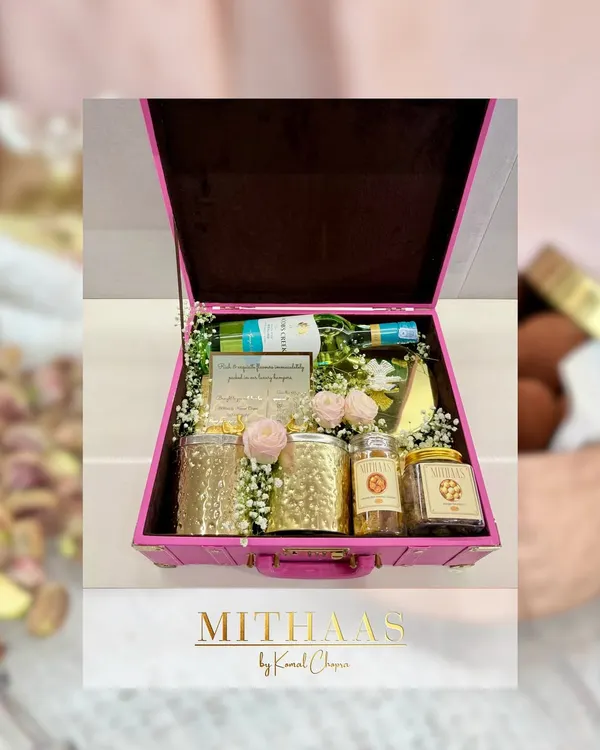 This custom hamper, built in a beautiful pink trunk, shows the variety you can choose from. It includes a bottle of non-alcoholic wine, jars of gourmet nuts, and a personalized note, all adorned with fresh roses.
