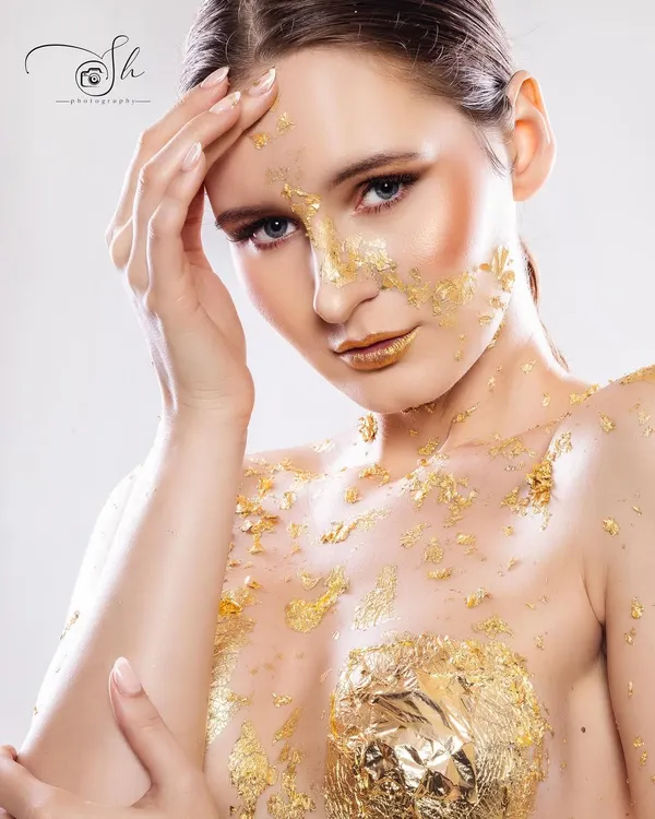 A stunning editorial shot featuring a model adorned with gold foil makeup. The artistic application and the model's intense expression create a high-fashion image that is both beautiful and memorable.