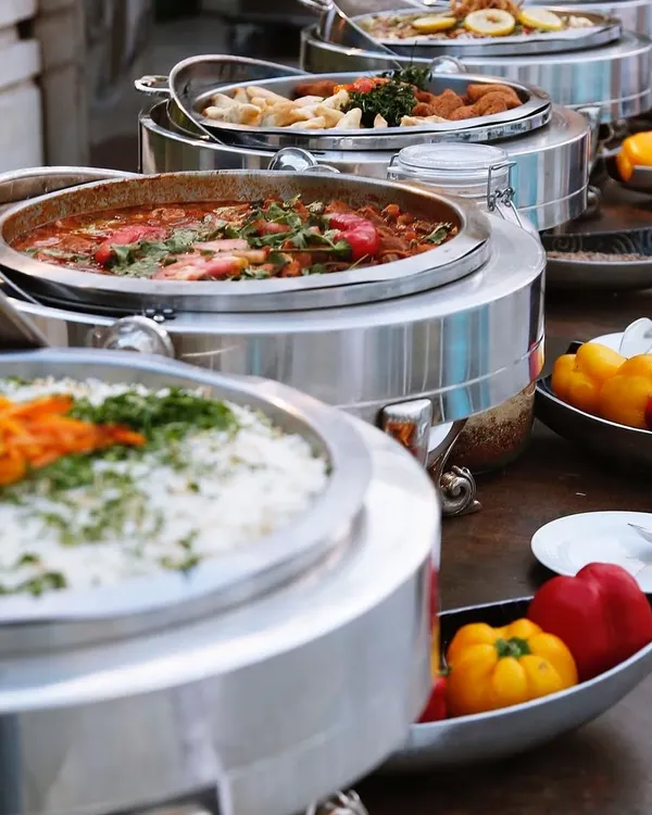 A beautiful shot of my buffet line, featuring a variety of main courses in gleaming silver chafing dishes. I use fresh ingredients, like the colorful bell peppers seen here, to add vibrancy and flavor to the spread.