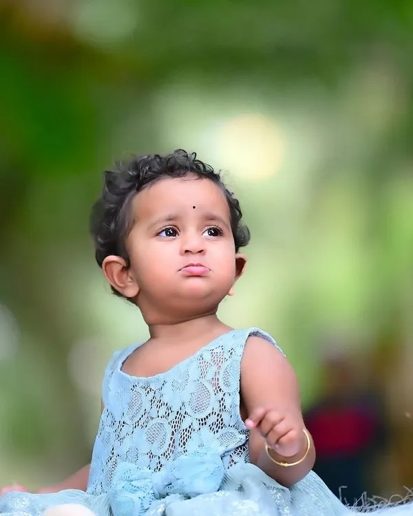 A beautiful outdoor portrait of a baby girl, lost in thought. The soft, natural background and her sweet expression make this a simple yet captivating image.