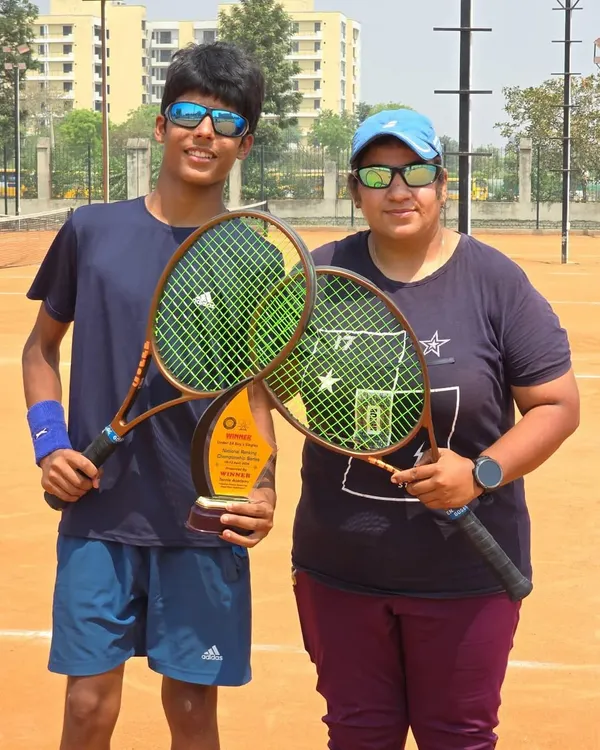 A milestone moment for Ayush Chaudhary, winning his first AITA National U-14 singles title. Here he is with his coach, holding their rackets and the winner's trophy on the clay court.
