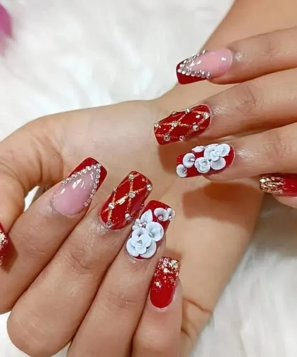 A full view of an extravagant bridal nail set, combining red polish, 3D white flowers, rhinestone patterns, and gold glitter accents for a truly luxurious look.