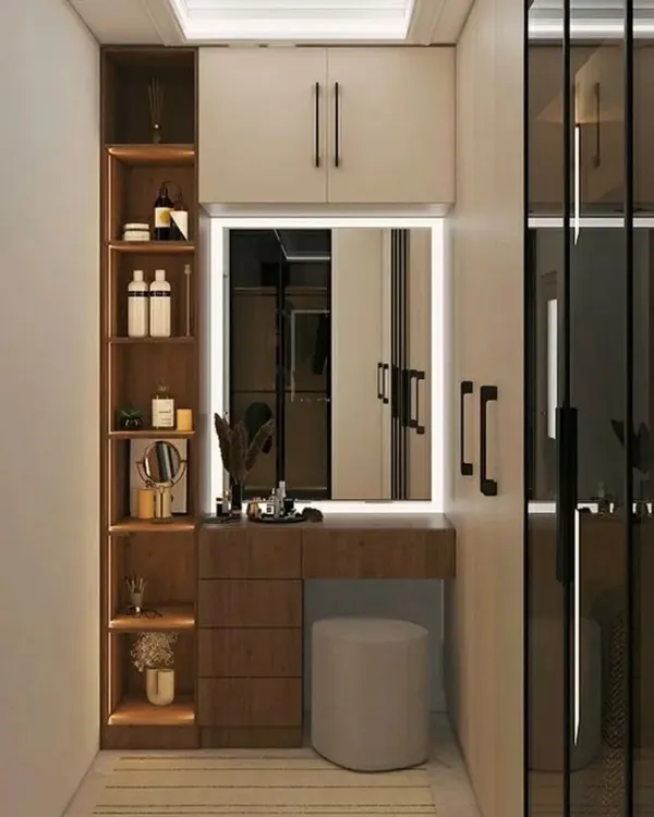 A compact dressing area with a built-in vanity and wardrobe. The illuminated mirror and open shelving provide a perfect spot for getting ready.