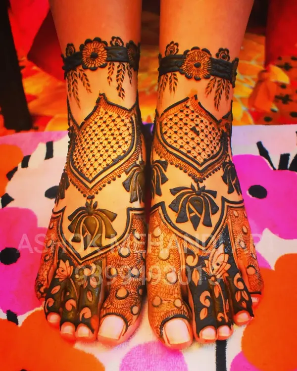 An elegant feet mehndi design featuring lotus motifs and intricate net patterns (jaal). The design creates a beautiful V-shape that elongates the feet.