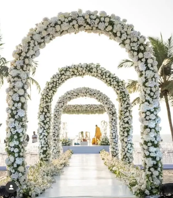 I designed this breathtaking wedding aisle with a series of grand arches made entirely of white flowers. This created a stunning walkway leading to the beachside mandap, making the bride's entrance truly unforgettable.