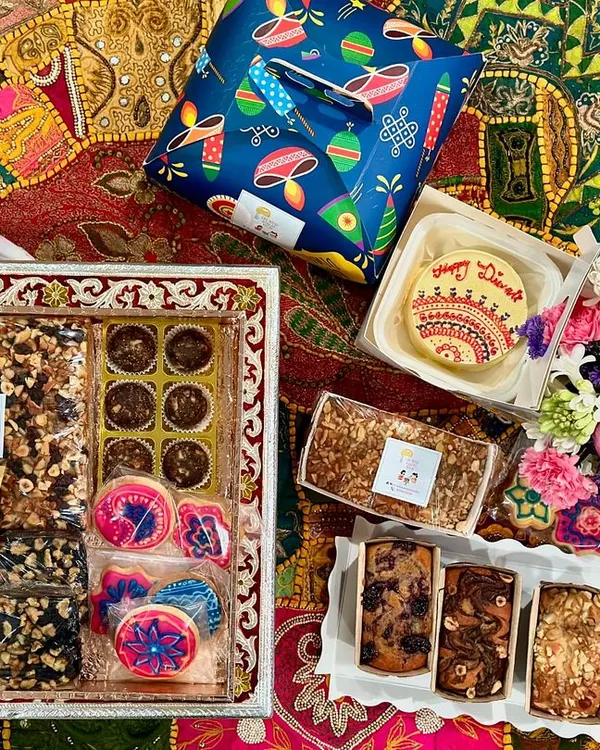 A complete celebration spread showcasing the variety we offer. This custom Diwali hamper includes a hand-decorated bento cake, assorted tea cakes, themed icing cookies, chocolate nut clusters, and fresh flowers, all arranged beautifully for gifting.