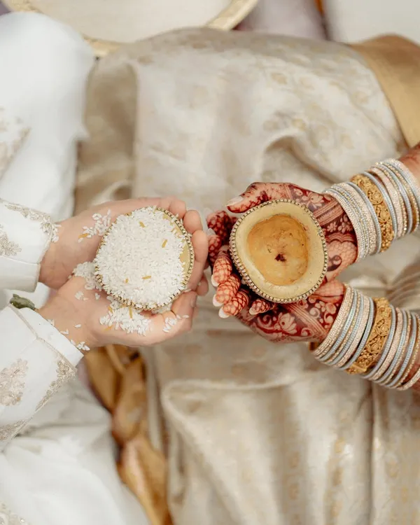 A close-up of a South Indian wedding ritual. This shot focuses on the hands of the couple, the intricate henna, and the symbolic offerings, capturing the beauty of the tradition.