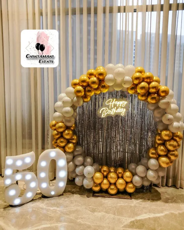 I designed this elegant setup for a 50th birthday party. The circular balloon arch in gold and white, paired with a custom neon sign and large light-up marquee numbers, creates a sophisticated and memorable photo backdrop for milestone celebrations.