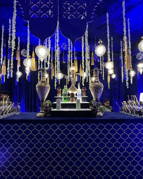 A wide view of our grand Sufi Night bar. The setup is defined by its rich royal blue fabric, intricate silver Moroccan patterns, and an elaborate overhead arrangement of hanging lights and tassels.