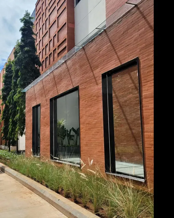 The facade of the Campus Biovet office block, where an entire wall is clad in exposed brick. The glass roof of the protruding entryway reflects the sky, creating a beautiful contrast between the earthy brick and the open air.