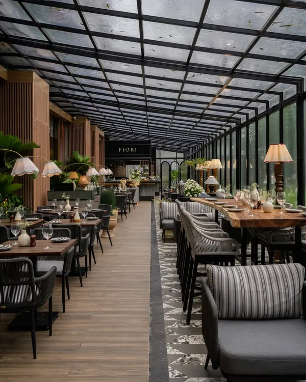 The dining space at FIORI, Lonavala, is designed to connect with its serene, verdant surroundings. A glass roof and walls create an al fresco feel, while the material palette of stone and wood-finished aluminum ensures durability and aligns with our sustainable practices.