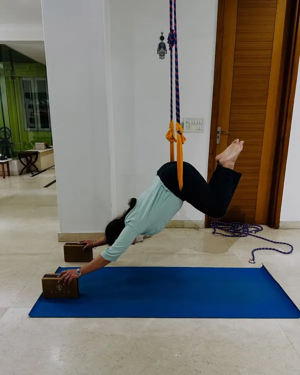 Wall ropes can transform your practice. Here, a student uses the ropes to decompress the spine and open the shoulders in a supported version of Downward-Facing Dog, making the pose more therapeutic.