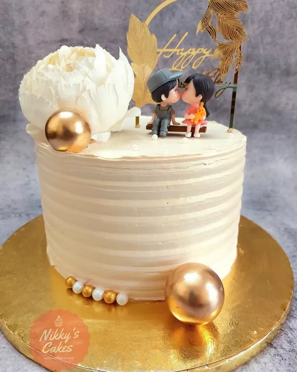This strawberry flavored cake is perfect for an anniversary or engagement. It features a clean, striped frosting finish, golden decorative spheres, and an adorable topper of a couple sharing a sweet moment.