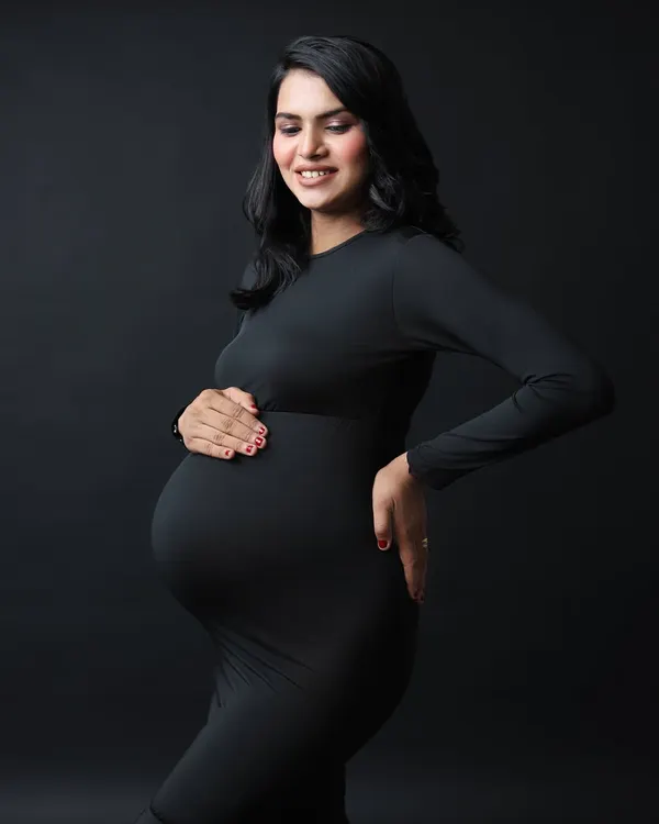 A classic solo maternity portrait. The simple black dress and dark background create a stunning, high-contrast image that beautifully highlights the baby bump.