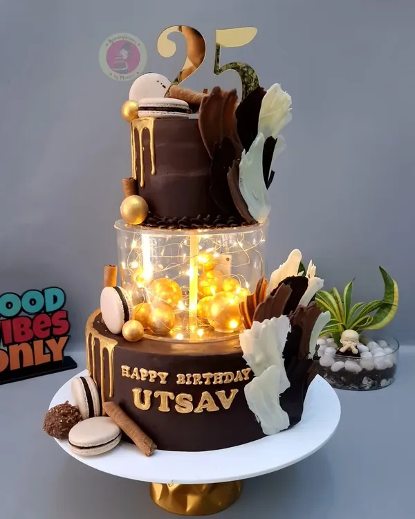A breathtaking two-tier chocolate cake with a lit-up separator, gold drip, and artistic chocolate sails. This cake is pure modern elegance.