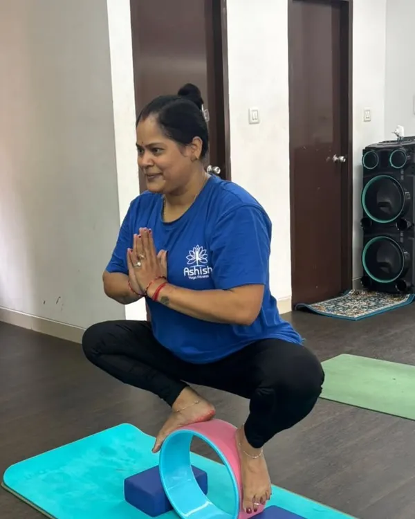 A student uses a yoga wheel and blocks for support in Malasana (Garland Pose), helping to open the hips while maintaining balance.