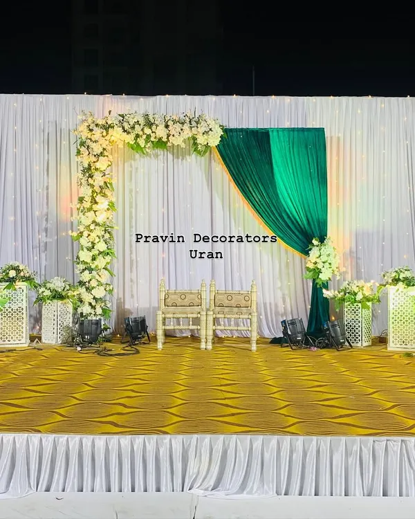 A classic stage setup for a Tilak ceremony. The design features an elegant floral arch of white roses against a backdrop of white and rich green drapes, creating a fresh and traditional look.