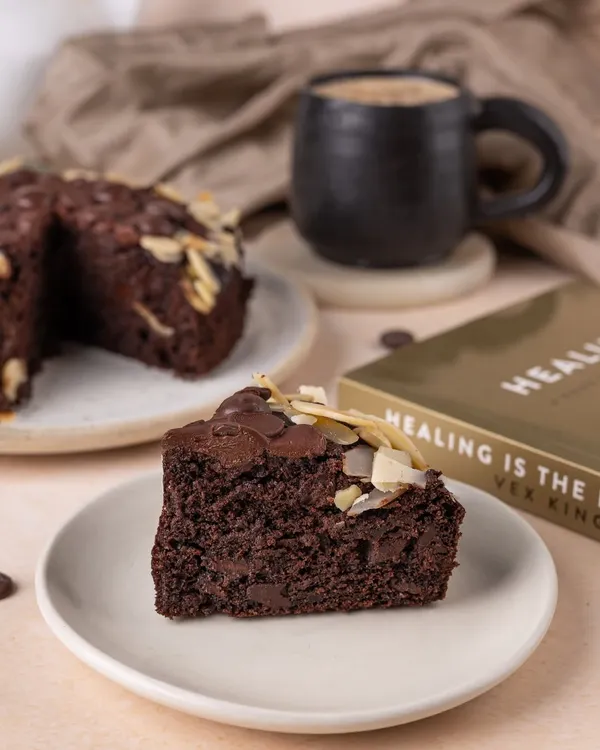 A perfect slice of chocolate almond cake paired with coffee, styled with a book to create a cozy, relaxing afternoon vibe.