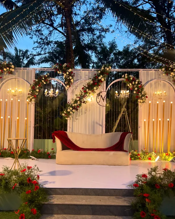 A beautifully lit stage for a wedding reception. The design features modern arches, floral arrangements in red and white, and elegant candelabras, creating a romantic focal point for the evening.