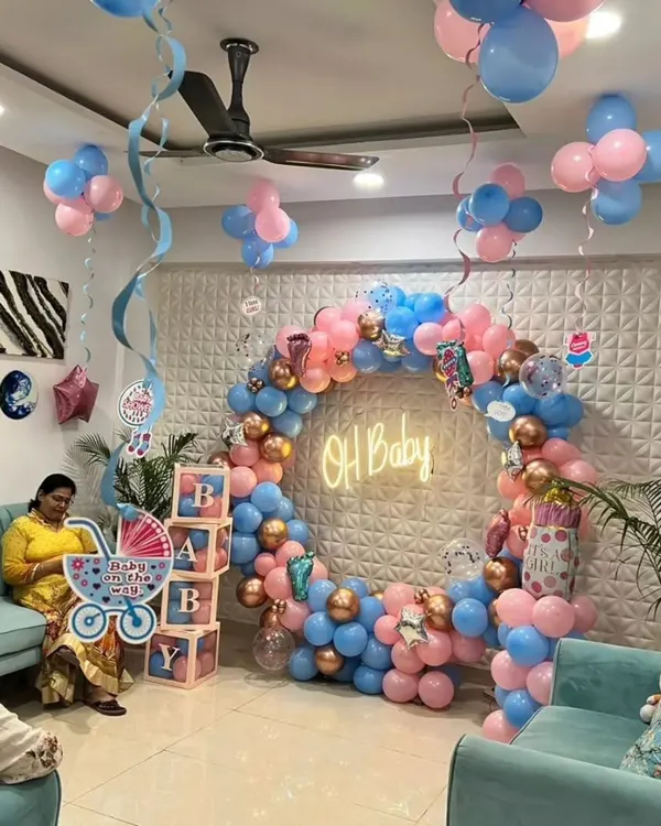 A full room setup for a baby shower. This includes a circular balloon arch with an 'Oh Baby' neon sign, 'BABY' display boxes, and balloon clusters on the ceiling.