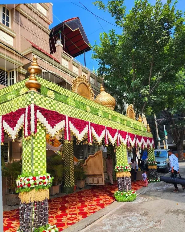 A complete view of a traditional wedding *chappara* I built. The structure is made from woven coconut leaves with a red and white flower border, and the pillars are decorated with sugarcane and flower bouquets.