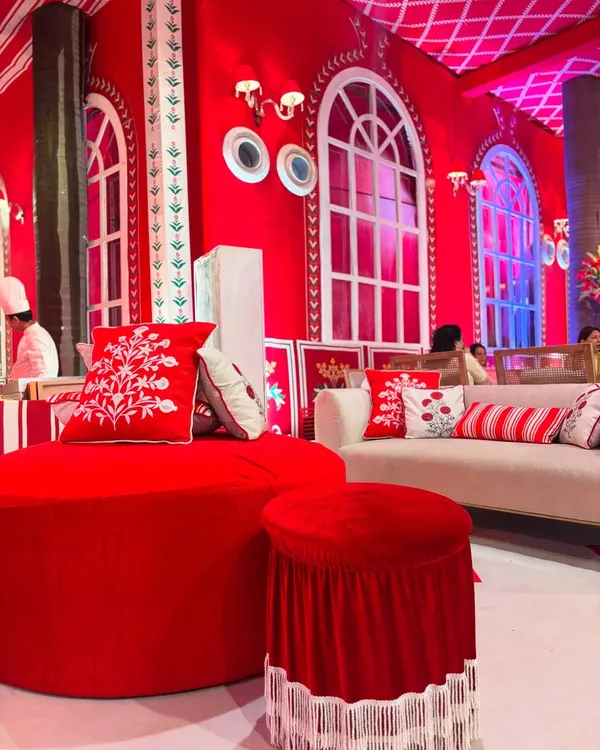 A comfortable and stylish seating lounge from the 'Laal Ishq' event. The vibrant red furniture, custom-embroidered cushions, and arched windows are all inspired by the iconic Villa Palladio in Jaipur.