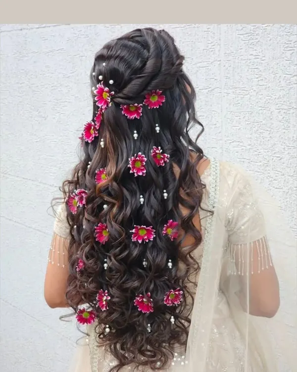 A stunning open hairstyle with cascading curls, decorated with bright pink flowers and pearls. This is a beautiful choice for a mehendi or sangeet ceremony.