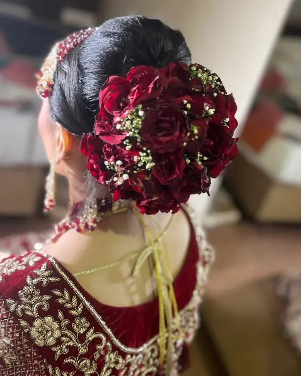A perfect view of a classic bridal bun, decorated with a circle of fresh red roses and baby's breath. This style is timeless and provides a sturdy base for any dupatta or veil.