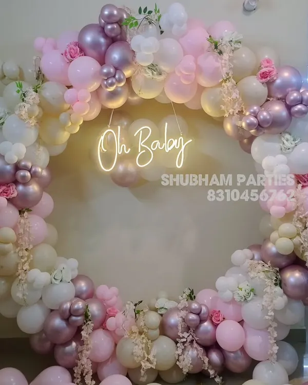 An elegant "Oh Baby" shower decoration featuring a circular balloon ring in pastel pink, white, and chrome, adorned with artificial flowers.